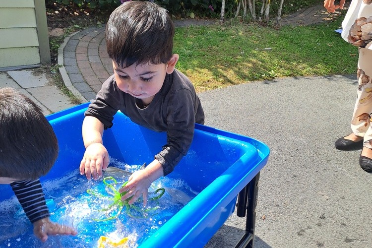 Two children playing in a water tub with colourful toys, splashing water.