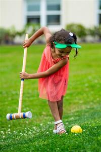 Girl with a wooden mallet aiming to hit a yellow ball.